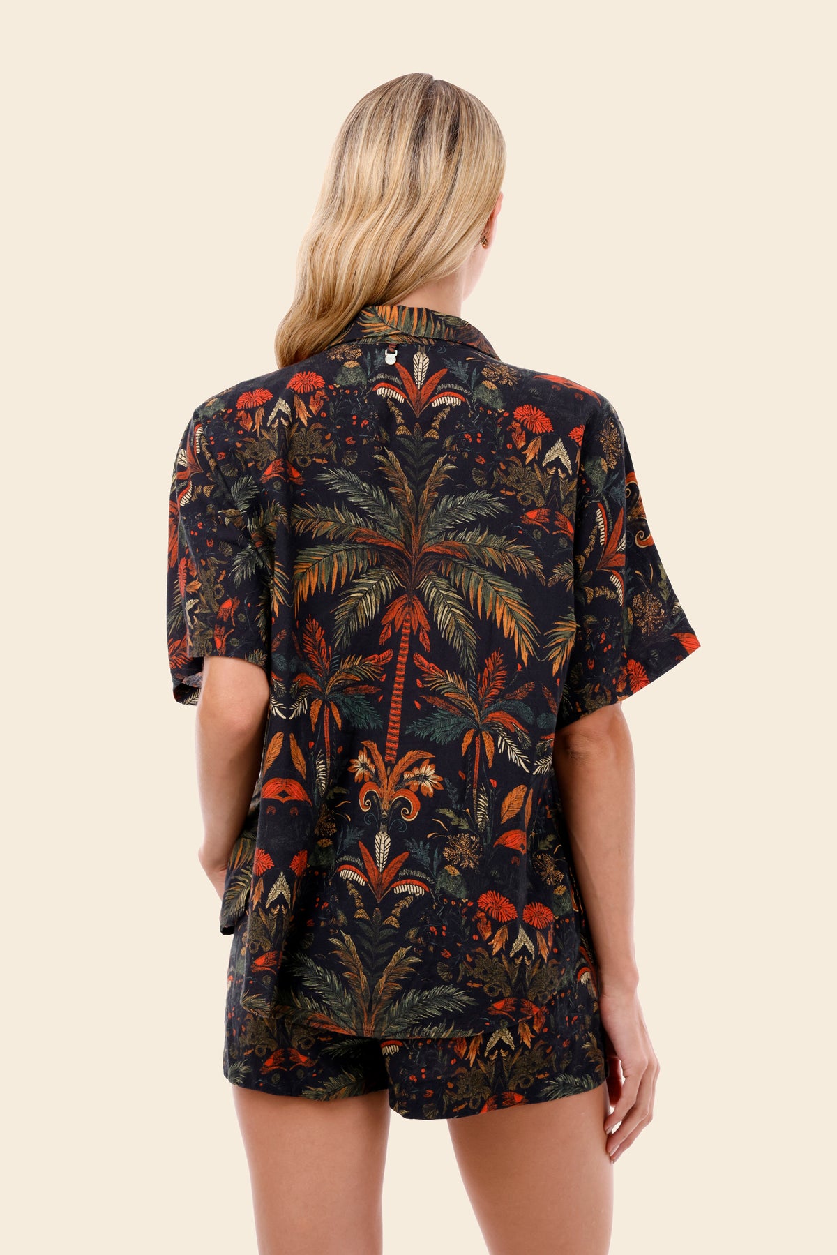 Person wearing a dark patterned outfit with palm tree design for resort wear for women on a beige background