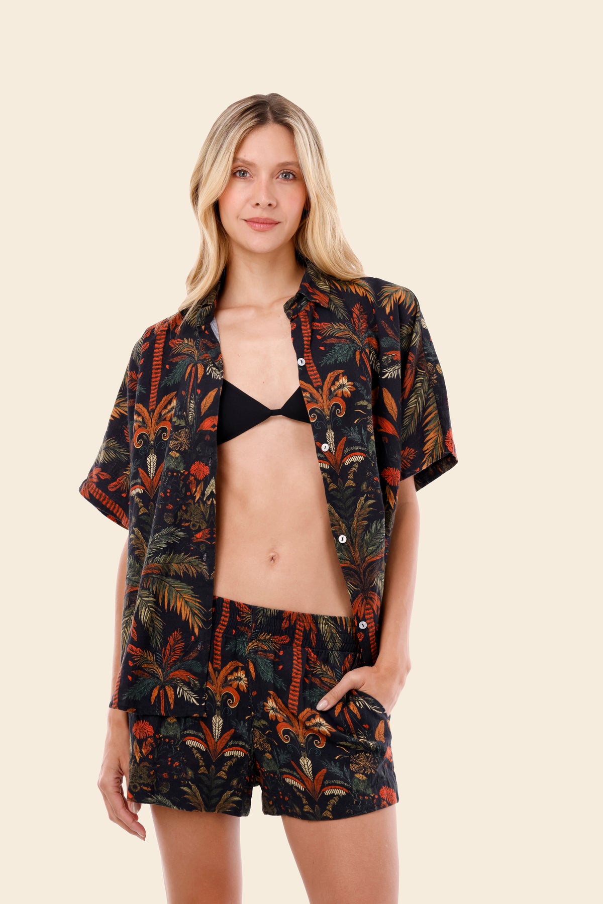 Woman wearing a patterned shirt, bikini top, and shorts on a beige background